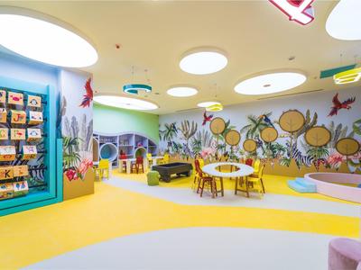 Bunter, großer Spielraum mit runden Tischen, Stühlen, Wanddekorationen und Spielzeugen für Kinder.