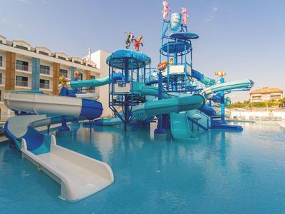 Wasserpark mit blauen Rutschen, türkisfarbenem Wasserbecken und Gebäuden im Hintergrund bei klarem Himmel.