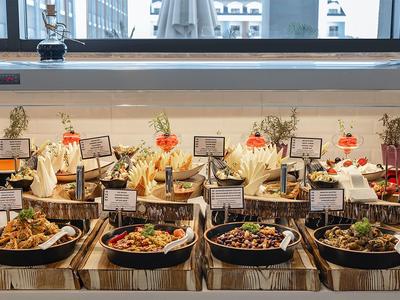 Buffet mit verschiedenen warmen Speisen in schwarzen Schalen, dekoriert mit Blumen und Beschriftungsschildern.