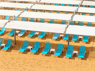 Blaue Liegestühle unter weißen Sonnenschirmen am Sandstrand.