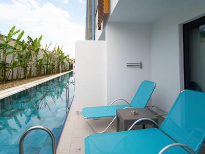 Zwei blaue Liegestühle neben einem schmalen Hotelpool mit Pflanzen entlang der Mauer.