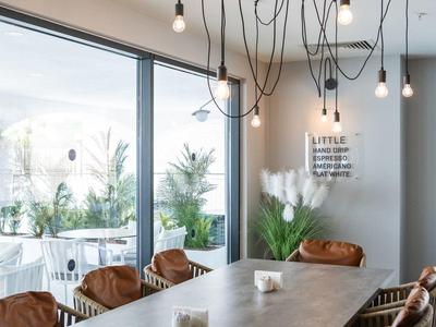 Moderner Essbereich mit langem Tisch, braunen Stühlen und hängenden Lampen neben großen Fenstern.