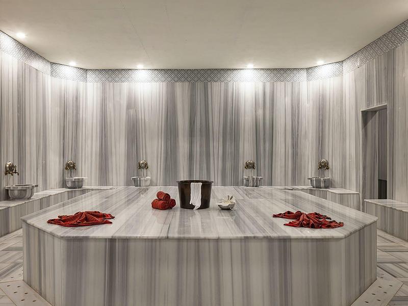 Großer, rechteckiger Marmor-Tisch in einem eleganten, hellen türkischen Hamam mit Handtüchern.