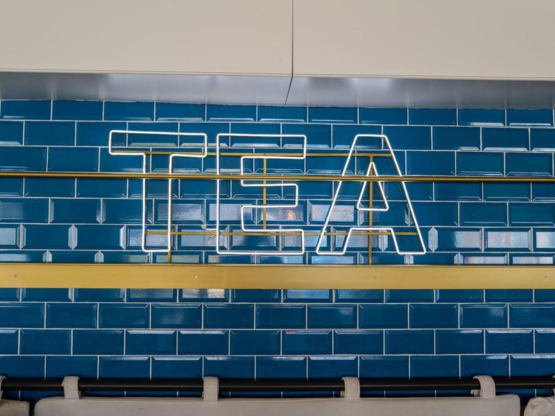 Leuchtendes TEA-Schild vor blauen Kacheln an einer Wand