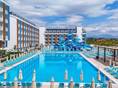 Grande piscine extérieure devant un hôtel moderne avec des transats et des toboggans bleus.