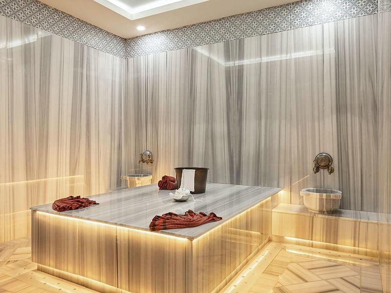 Elegancka, oświetlona strefa wellness z marmurowym stołem i ciepłymi drewnianymi akcentami.