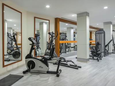 Nowoczesna siłownia z lustrami, sprzętem do ćwiczeń i jasną podłogą.