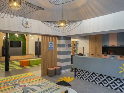 Nowoczesna lobby hotelowa z recepcją, kolorowym dywanem i częścią wypoczynkową z półkami.