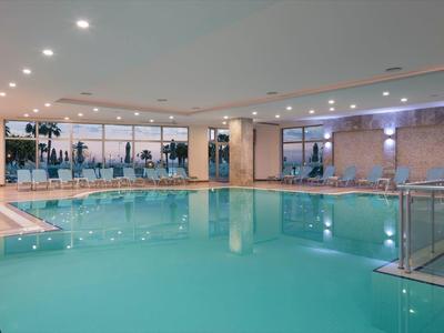 Kryty podgrzewany basen hotelowy z leżakami i dużą szklaną ścianą.