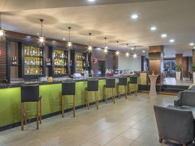 Nowoczesny bar hotelowy z zielonymi stołkami barowymi i przytulnymi kącikami do siedzenia.