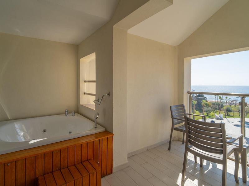 Balkon z jacuzzi, stołem i krzesłami z widokiem na morze i ogród.