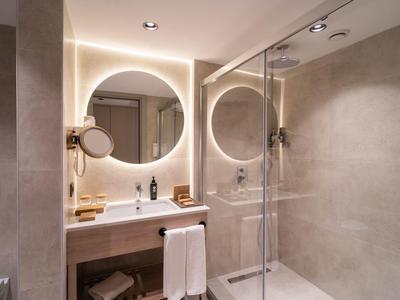 Salle de bain moderne avec miroir rond, lavabo et grande douche à l'italienne.