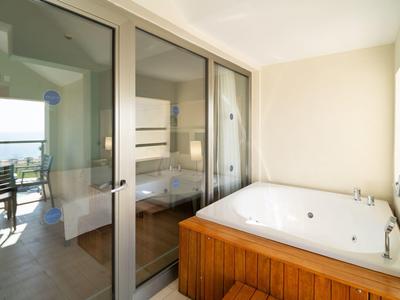 Salle de bain lumineuse avec baignoire en bois et balcon offrant une vue sur la mer.