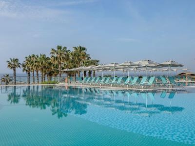 Modern pool area with sun loungers near palm trees at a hotel with sea view.