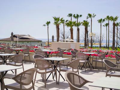 Terrasse vide avec chaises et tables, palmiers et vue sur la mer en arrière-plan par temps clair.