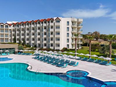 Large hotel pool with sun loungers and multi-story hotel building in the background under clear sky.