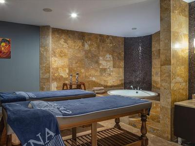 Wnętrze pokoju zabiegowego spa z łóżkiem do masażu i umywalką, ciepłe oświetlenie