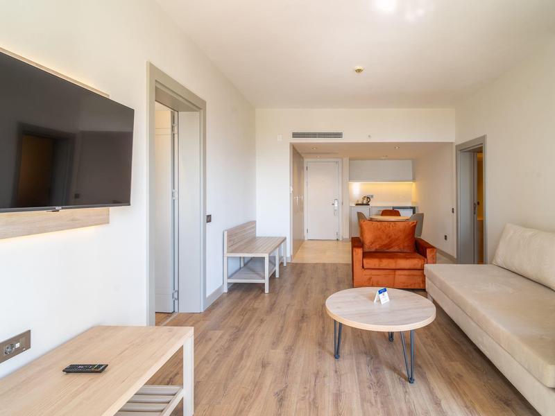Chambre d'hôtel moderne avec canapé, télévision et table basse sur sol en bois.