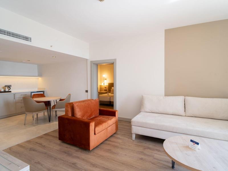 Salon moderne avec mobilier beige et marron et vue sur la cuisine.