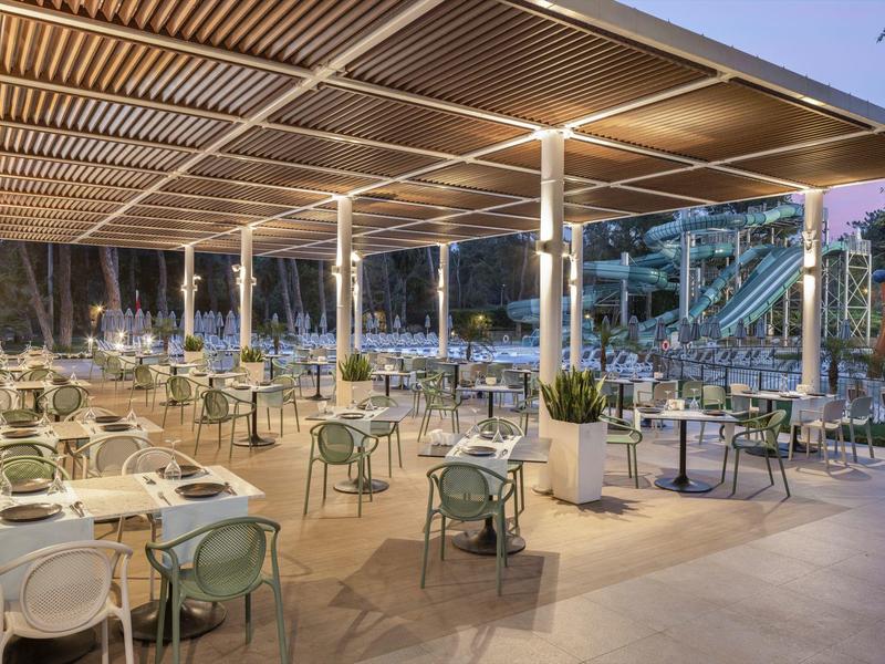 Grande terrasse de restaurant extérieure avec tables dressées et éclairage moderne en soirée.