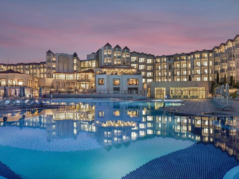 Grand hôtel avec piscine éclairée au crépuscule et ciel rose-violet.