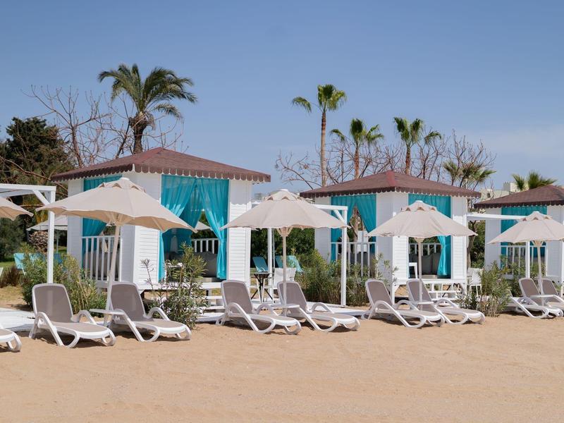 Plage avec des transats blancs et parasols devant de petites huttes bleues et blanches.