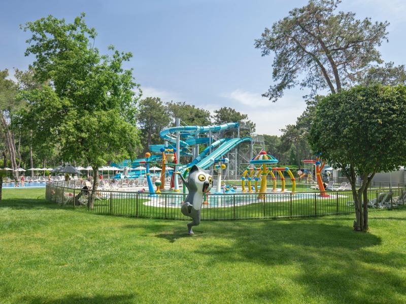 Aire de jeux aquatique avec toboggans et balançoires entourée de pelouse verte et d'arbres