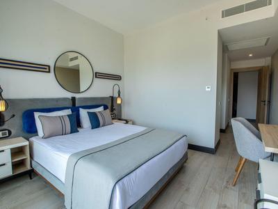 Modern hotel room with double bed, round mirror, desk, and neutral tones.