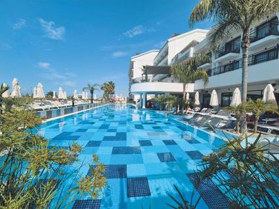 Large outdoor pool with blue patterned tiles and lounge chairs beside a modern hotel.