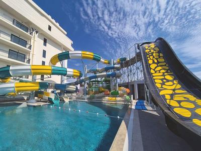 Outdoor pool with large colorful water slides next to a hotel building under a blue sky.