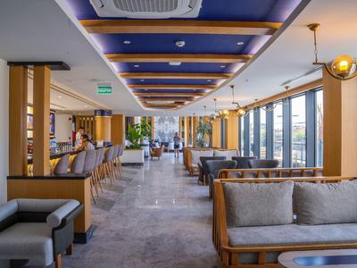 Bright, modern hotel lounge with wooden furniture, gray seats, and large windows.