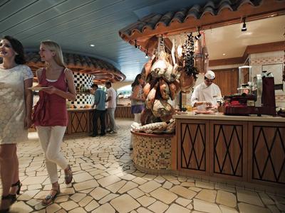 Two women walking in a restaurant with a chef preparing food behind the counter.