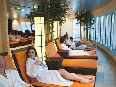 People in bathrobes relax on loungers in a panoramic room with large windows.