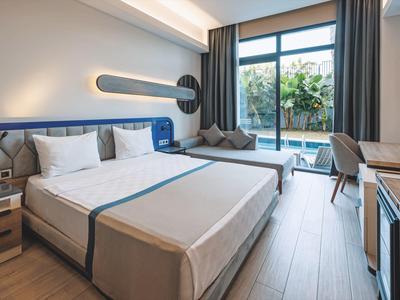 Camera d'hotel moderna con letto matrimoniale, scrivania e vista su terrazza con piante.