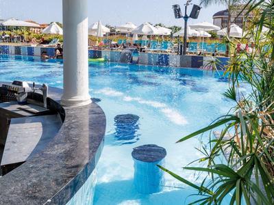 Piscina dell'hotel con sgabelli sommersi, ombrelloni e lettini sotto il sole.