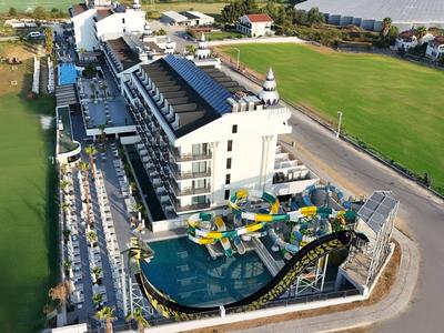 Complesso alberghiero moderno con scivoli d'acqua e campo sportivo verde accanto.