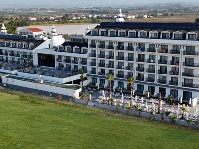 Grande edificio alberghiero su più piani con piscine, circondato da prati verdi.