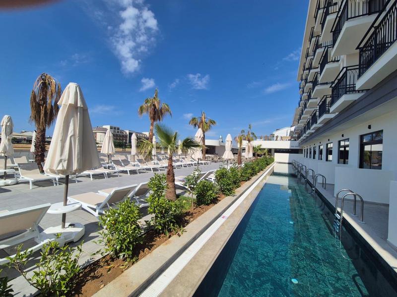 Piscina d'hotel moderna con palme e lettini sotto un cielo azzurro.