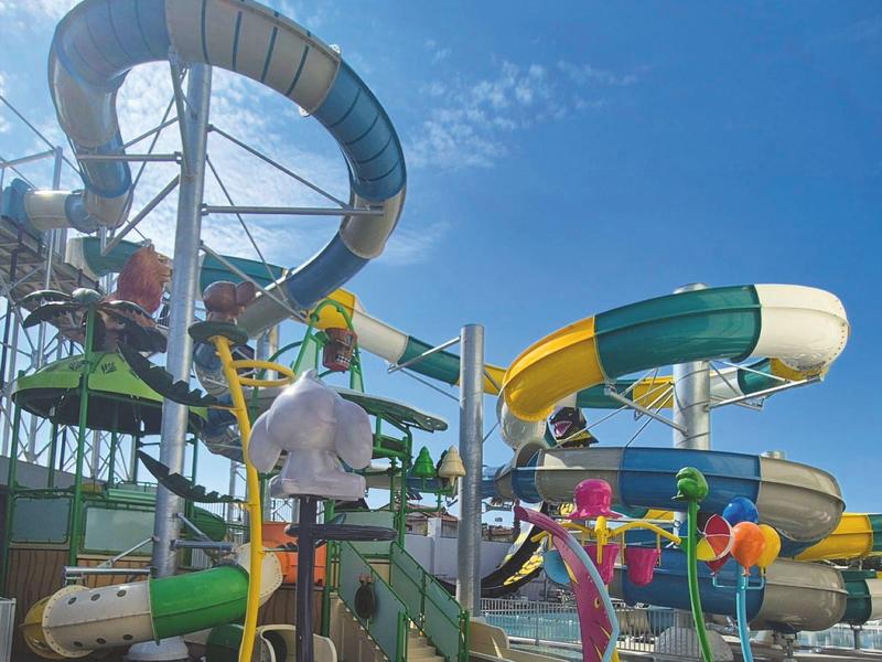 Parco acquatico con scivoli colorati e figure sotto un cielo azzurro