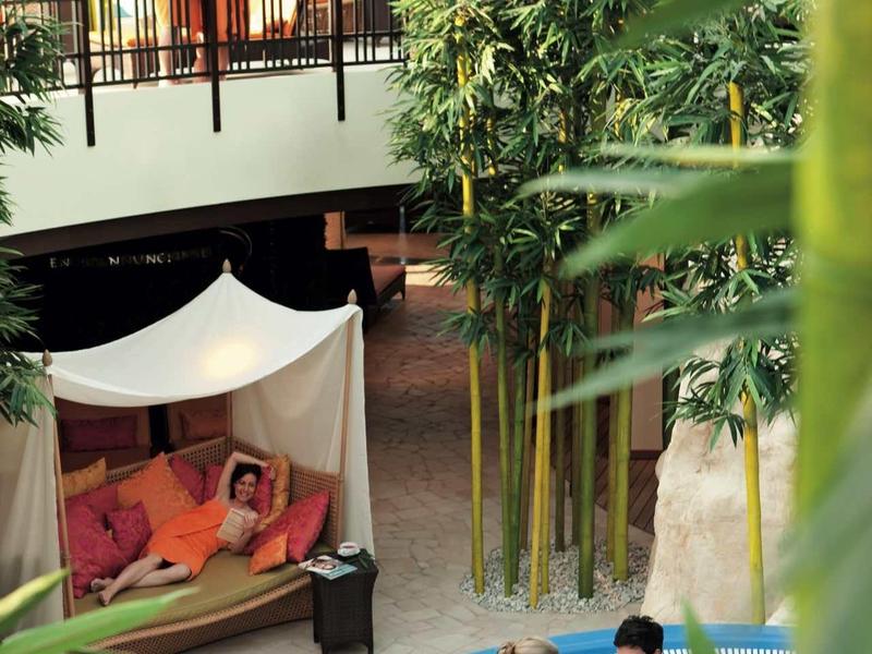 Area interna dell'hotel con piscina, piante di bambù e ospiti rilassati.