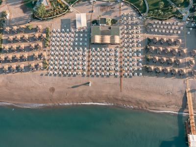 Widok z powietrza na plażę z rzędami parasoli i leżaków oraz pomostem wychodzącym na wodę.