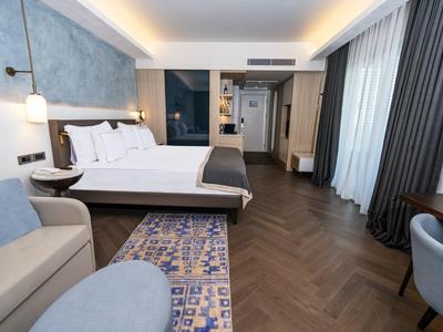 Nowoczesny pokój hotelowy z podwójnym łóżkiem, sofą i dużym oknem z zasłonami.