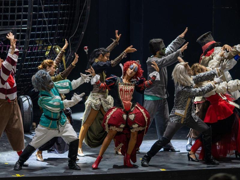 Kilku aktorów w kolorowych kostiumach wykonuje żywą scenę na scenie.