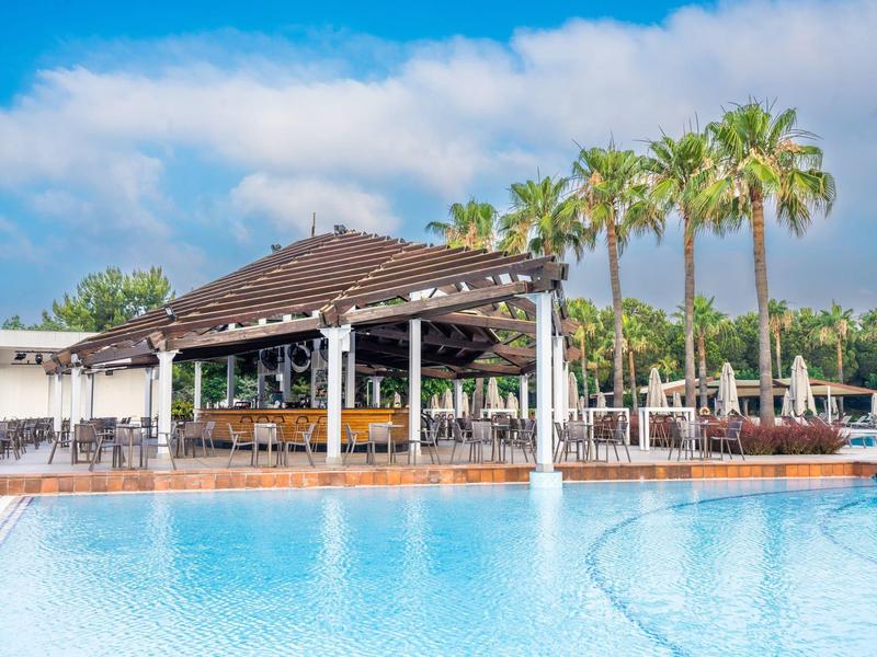 Basen hotelowy z parasolami, palmami i barem przy basenie pod niebieskim niebem.