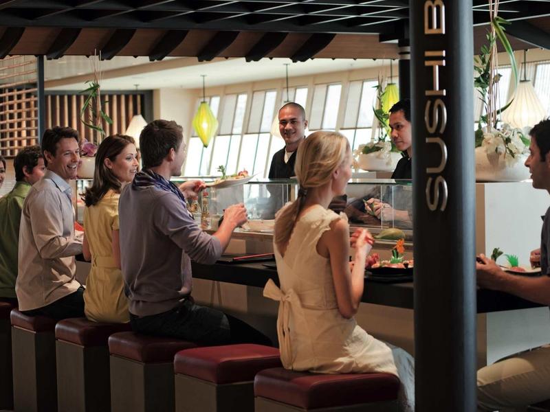 Ludzie siedzą przy barze sushi i piją napoje w relaksującej atmosferze.