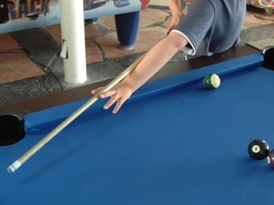 Garçon jouant au billard, visant avec la queue sur les boules.