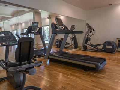 Salle de sport moderne avec tapis roulant, appareils d'entraînement et sol en bois.