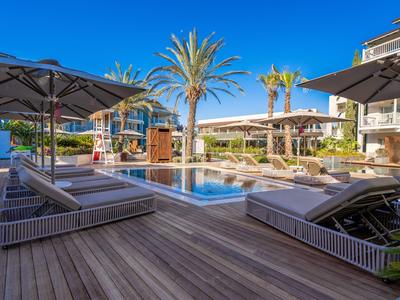 Modern hotel met zwembad, ligbedden en palmbomen onder een blauwe lucht.