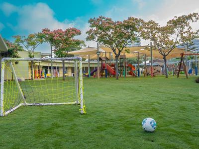 Boisko do piłki nożnej z bramką i piłką na zielonej trawie na zewnątrz obok placu zabaw.
