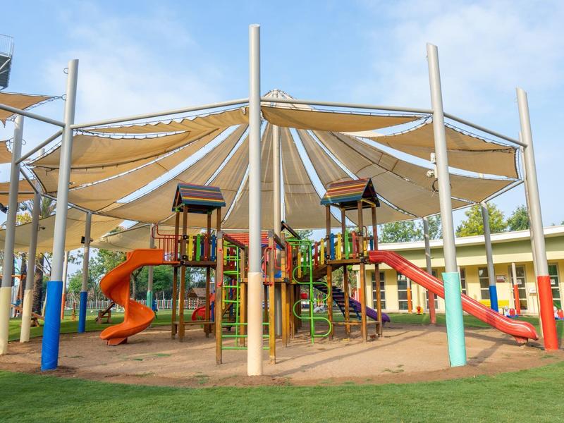 Kolorowy plac zabaw z zjeżdżalniami i żaglami przeciwsłonecznymi w hotelowym ogrodzie.